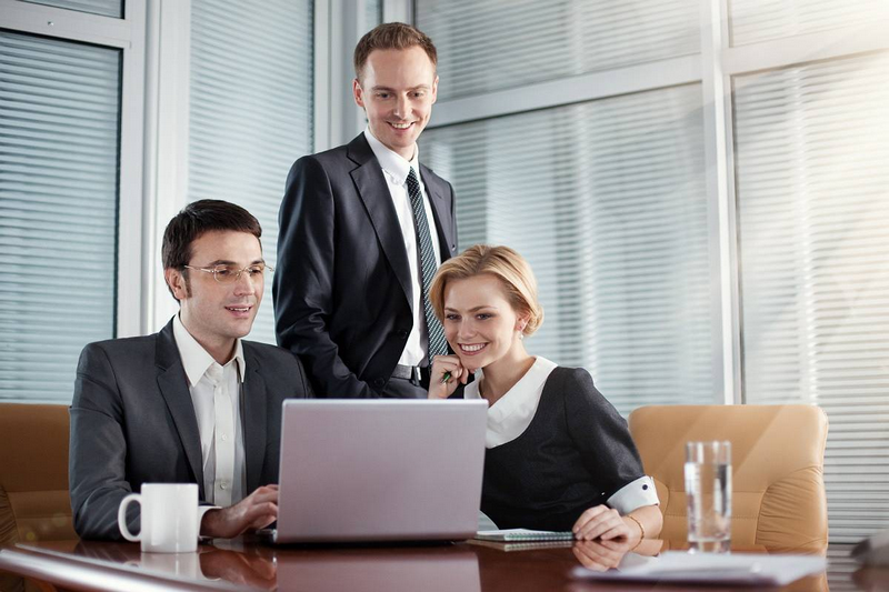 Three business people happily collaborating around a laptop in an office setting.