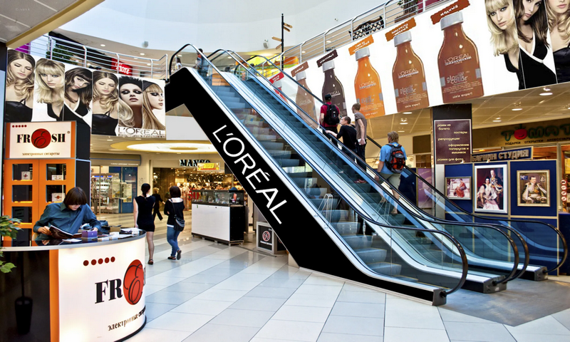 People use an escalator decorated with L'Oréal branding in a bustling shopping mall.