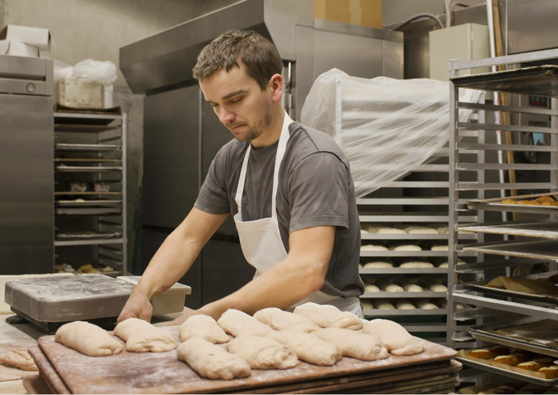 A baker prepares bread dough in a kitchen.